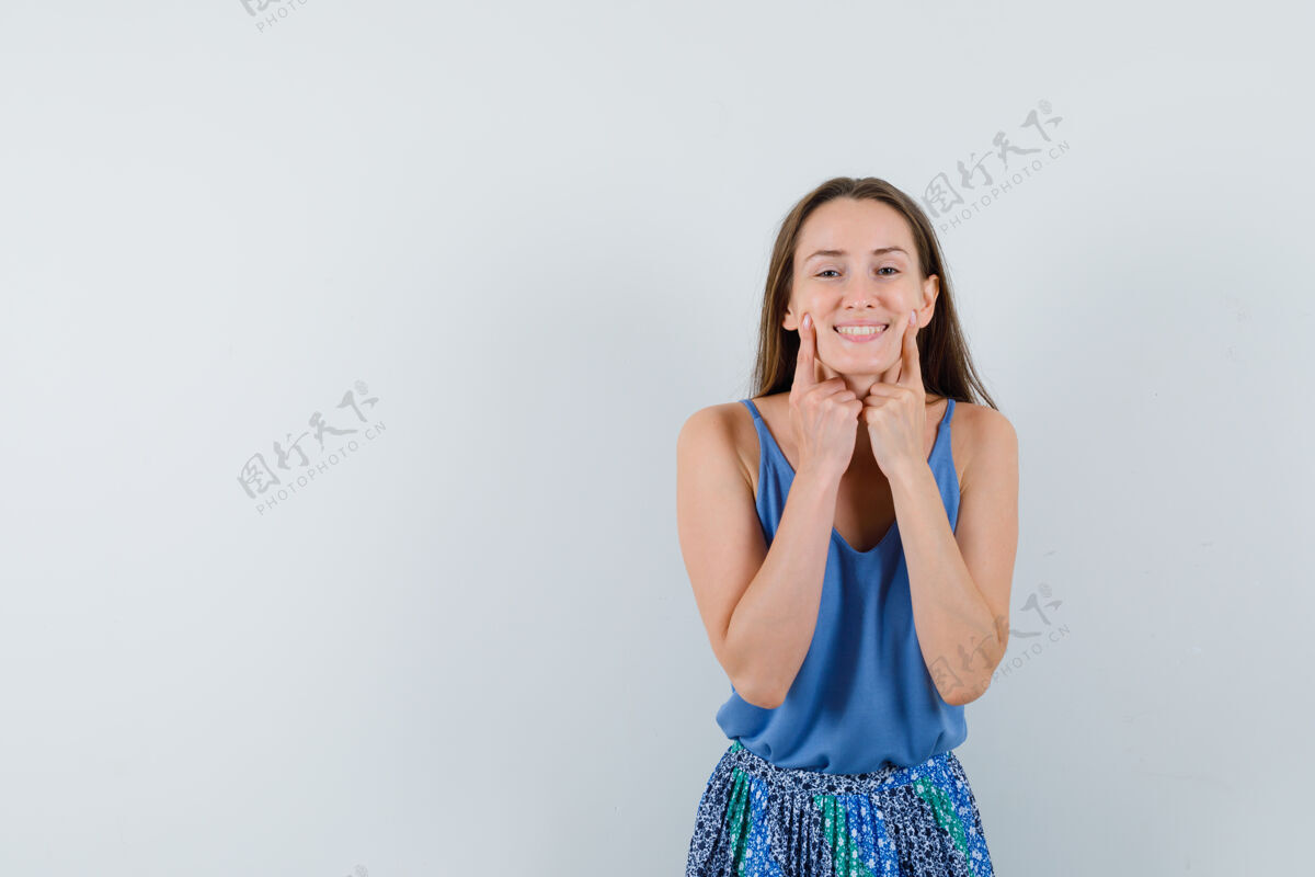 女孩年轻的女士指着她的微笑 穿着蓝色上衣 裙子 看起来兴高采烈 正面视图文本空间衬衫头发肖像