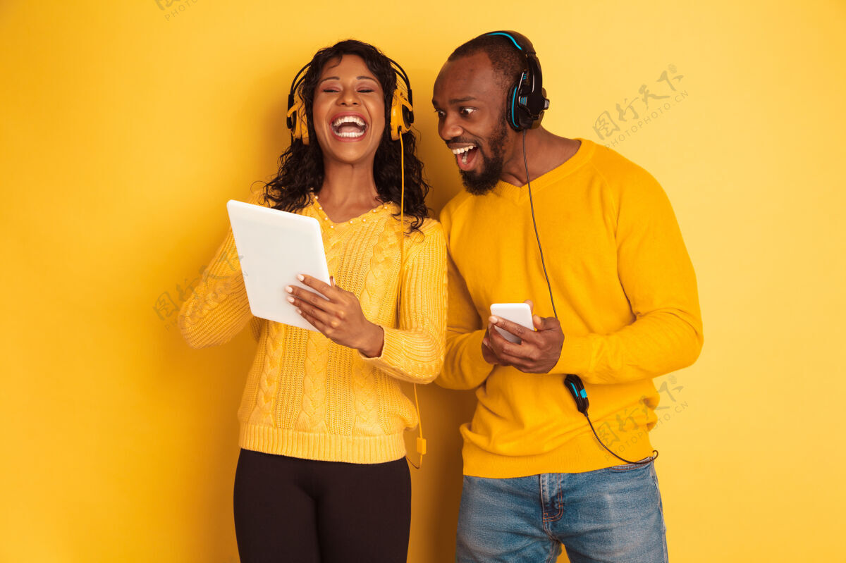姿势年轻感性的非裔美国人 穿着黄色背景的明亮休闲服美丽的情侣人类情感的概念 面部表情 关系 广告使用平板电脑和智能手机面部人非洲