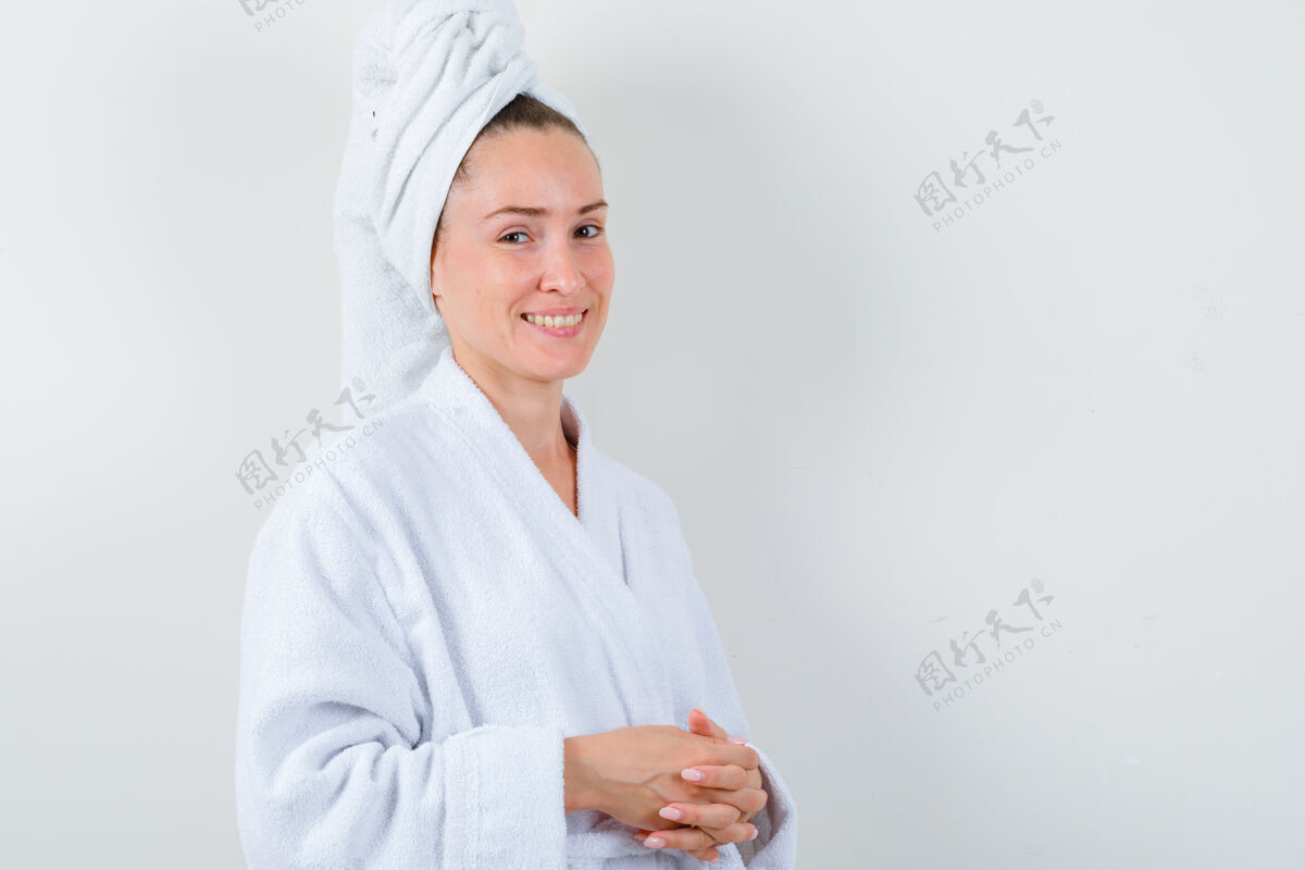 头发年轻的女士拿着白色浴衣 毛巾和她的手指在她面前合十 看起来很高兴 前视图人成人手指