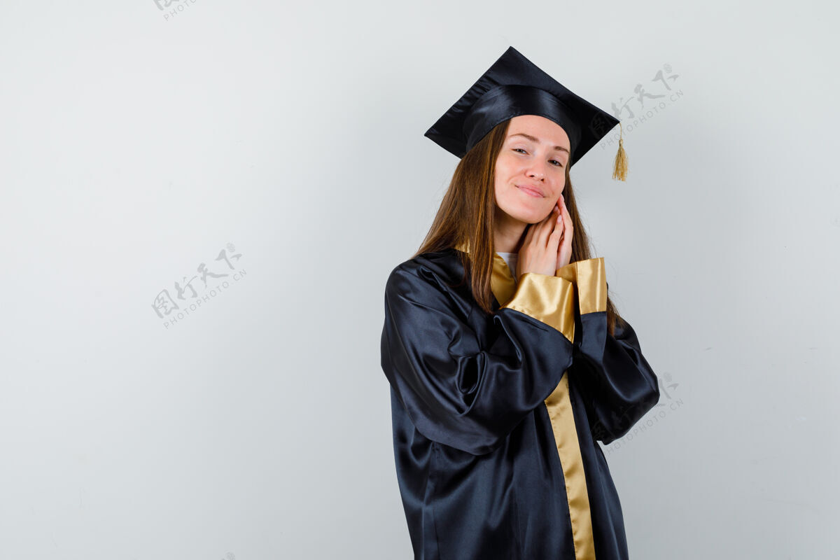 持有年轻的女毕业生手拉着脸颊 穿着学院服 看起来很漂亮正面图时尚前面学术