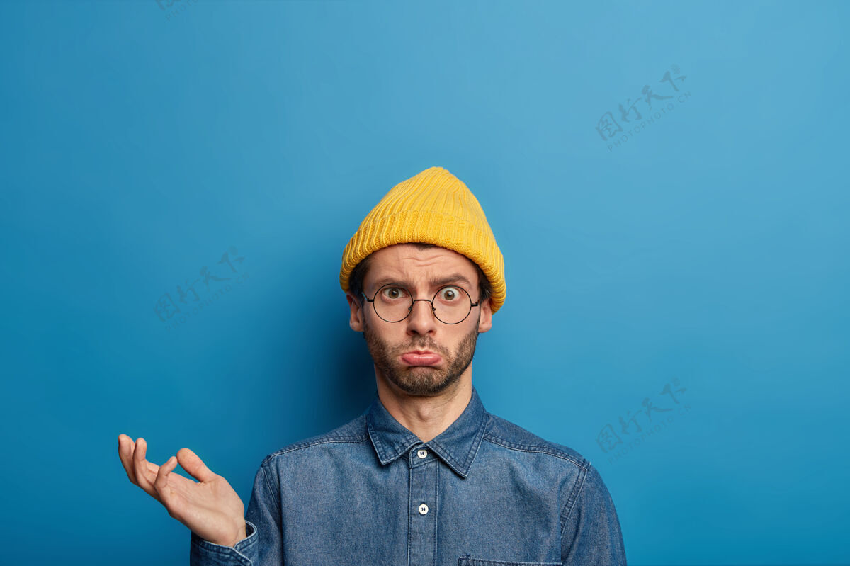 消极心烦意乱男子的照片抬起手掌 神情烦躁悲伤 戴着黄色帽子 牛仔衬衫衬衫时尚时尚