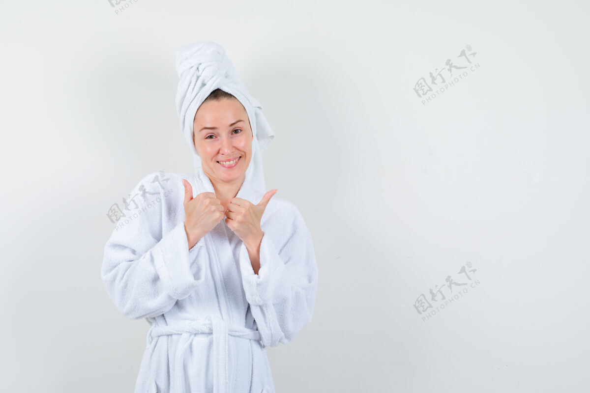 魅力身穿白色浴袍的年轻女子 毛巾上竖起大拇指 看上去很欢快 正前方的景色毛巾显示黑发