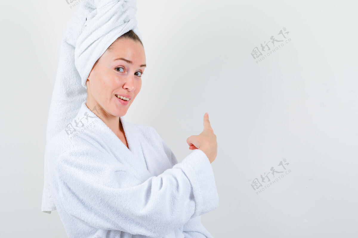 模特年轻的女士指着后面的白色浴衣 毛巾 看起来很快乐前视图完美健康清洁