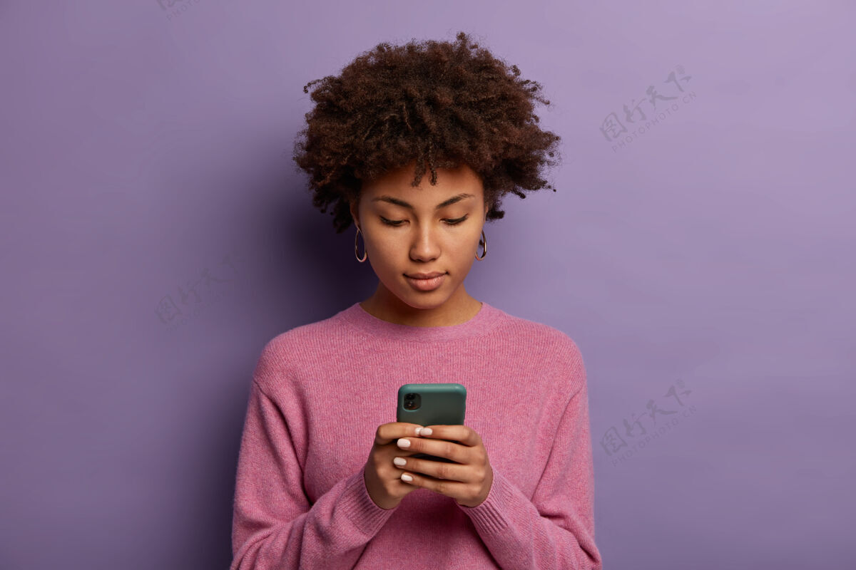 打字外表严肃的非裔美国妇女在现代手机上阅读信息 浏览社交媒体 在显示器上有集中的目光 穿着休闲套头衫非洲裔皮肤网络