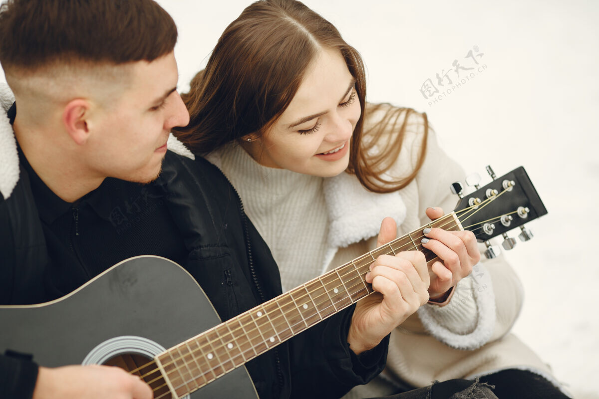 松树一对夫妇坐在雪林中的生活方式照片人们在户外度过寒假一对夫妇带着吉他女孩人白色