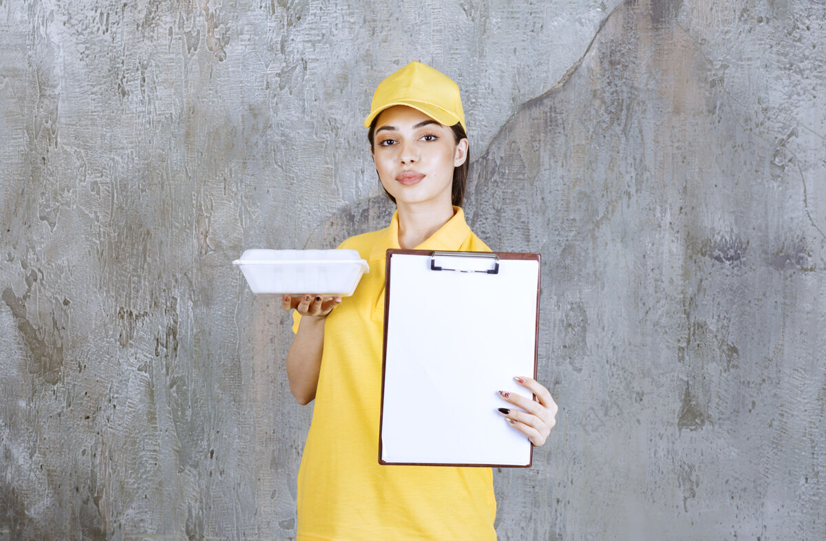 成人穿着黄色制服的女服务人员拿着一个塑料外卖盒 要求签名邮件清单年轻人