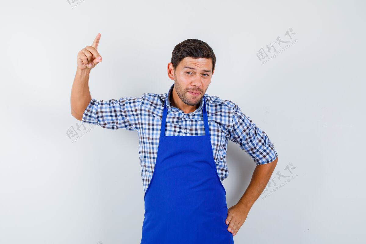 烹饪穿着蓝色围裙和衬衫的年轻男厨师男士男士衬衫