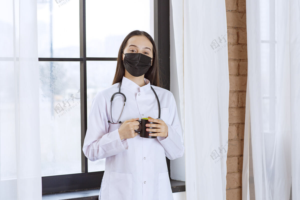 感冒医生带着听诊器和黑色口罩 在休息时端着一杯黑色饮料 暖手治疗医学从业者