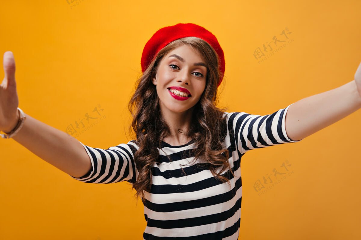 牛仔裙身着条纹衬衫和明亮贝雷帽的积极女性自拍戴着红帽子的时髦发型的酷女孩在孤立的背景上拍照女性黄色年轻