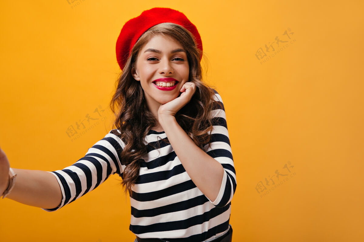 紫色戴着红色贝雷帽的酷女人微笑着自拍漂亮的年轻女人 戴着时髦的帽子和条纹衬衫摆姿势自拍牛仔裙橙色
