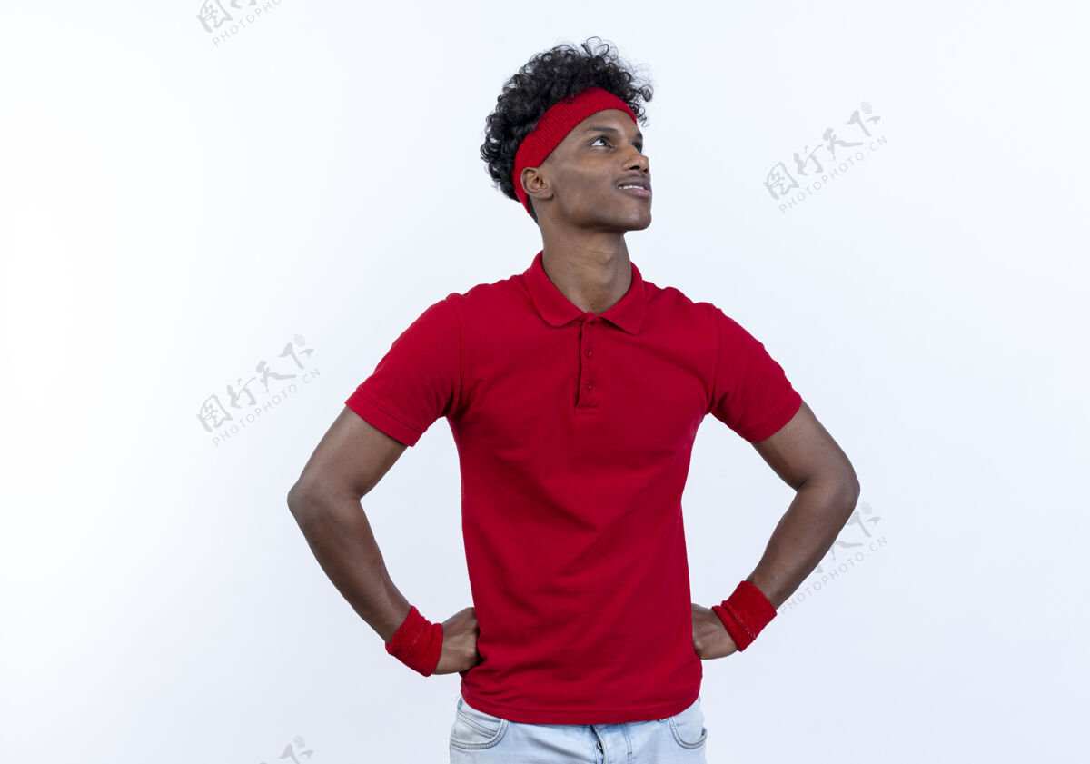 请穿看着身边高兴的年轻黑人美国运动男子戴着头带和腕带把双手放在臀部隔离在白色背景腕带手头带