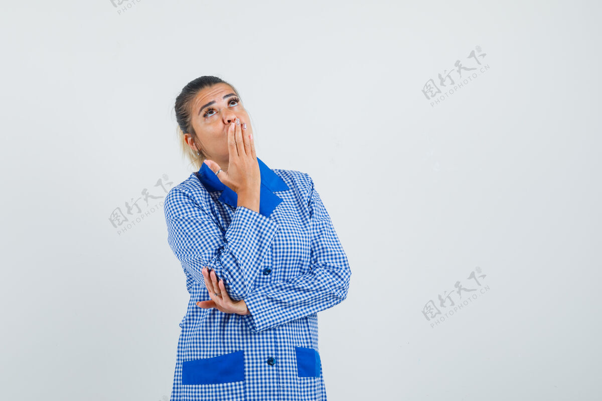 化妆年轻女子手放在嘴上 穿着蓝色方格布睡衣 站在思考的姿势 神情沉思前视图前面思考手