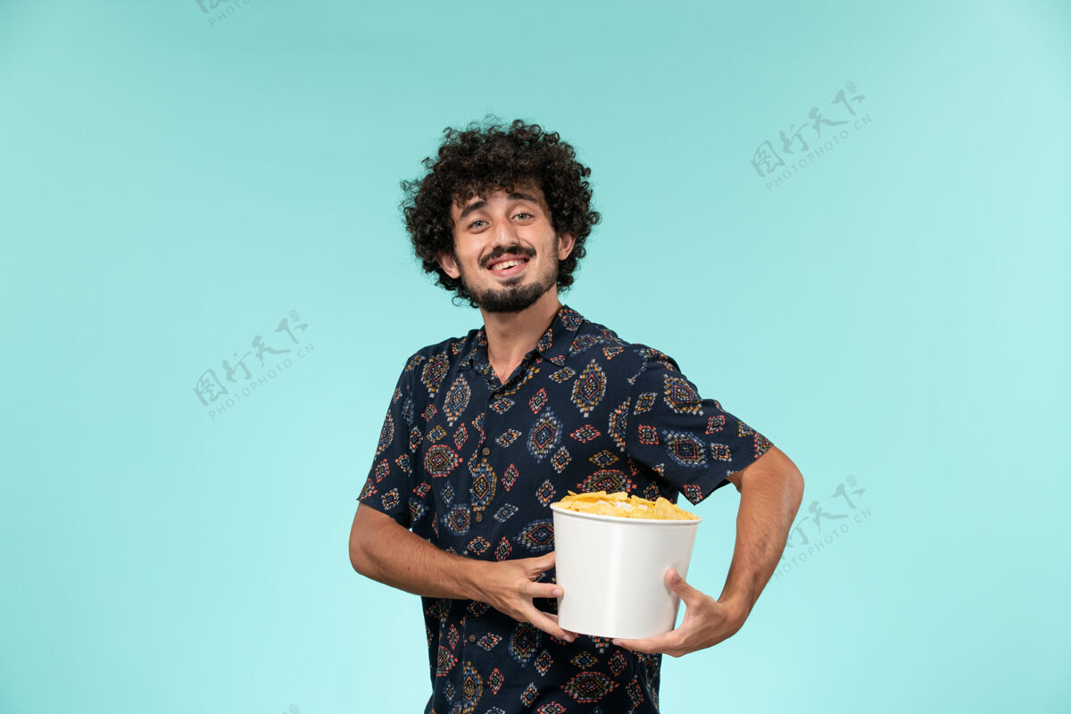 电影正面图：年轻人拿着篮子 手里拿着土豆 微笑着站在一个蓝色的墙边的电影院里容器微笑潘趣