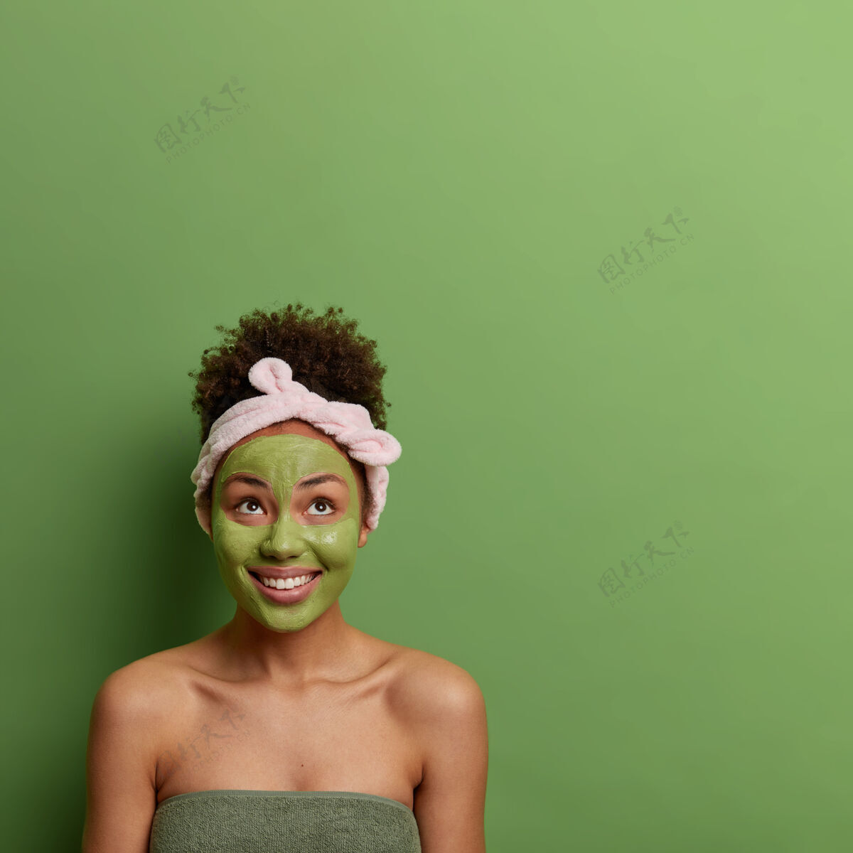 治疗Spa美容护肤理念积极的女性涂上去皮面膜 保持年轻美丽 面带笑容 戴上头巾 在绿色墙面上摆姿势个人空白治疗