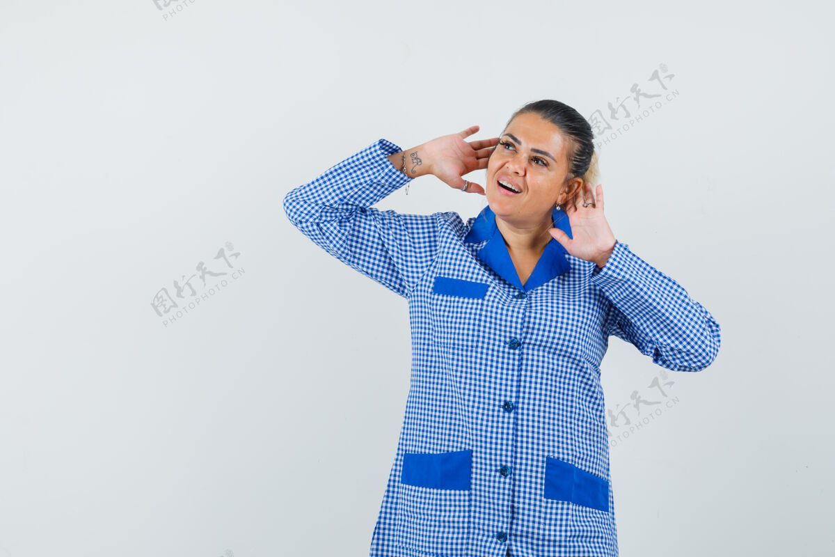 护理穿着蓝色方格睡衣衬衫的年轻女子把手放在耳边 听着某人说话 看上去很漂亮 正对着窗外看女性人新鲜