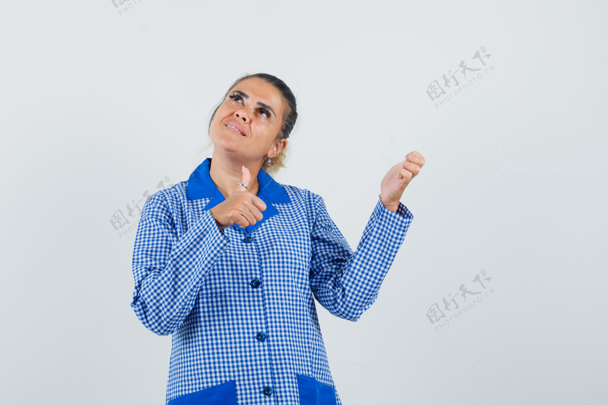 女性穿着蓝色方格布睡衣衬衫的年轻女子竖起大拇指举手 看起来很漂亮正视图年轻护理拇指