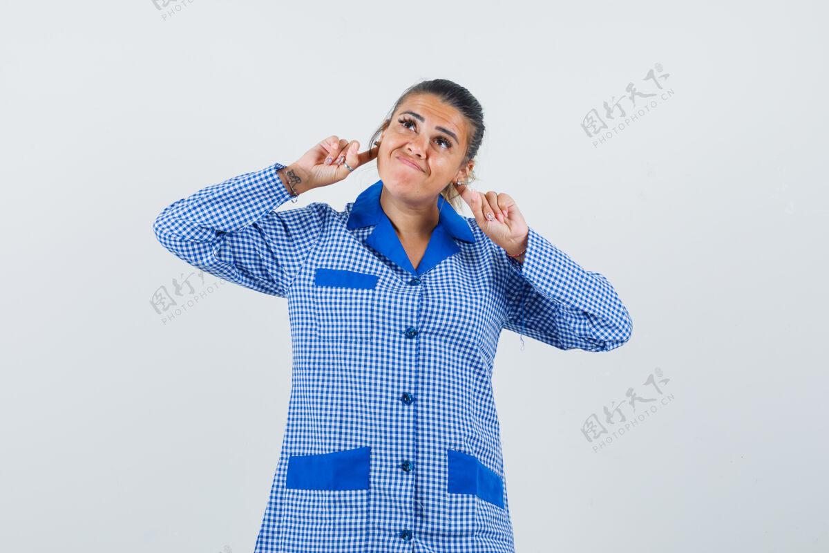 脸年轻女子拿着食指在耳后蓝色方格睡衣衬衫 看起来很漂亮 前视图肖像成人女孩