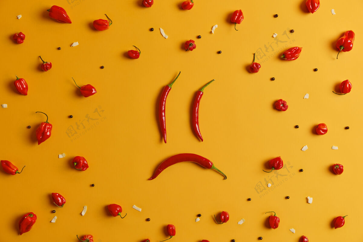 不高兴用长红辣椒做成的悲伤的人的脸 周围有胡椒的哈巴内罗辣椒 黄色的背景创意拍摄 食物艺术概念含有有益营养的辛辣成分辣味蔬菜生的空品种