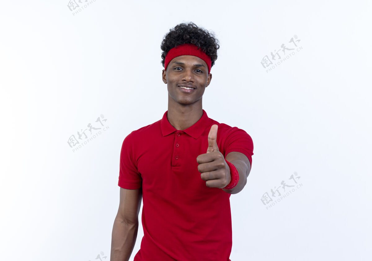 拇指戴着头带和腕带的年轻的美国黑人运动型男人很高兴 他的大拇指孤立地竖立在白色背景上年轻非裔美国人腕带