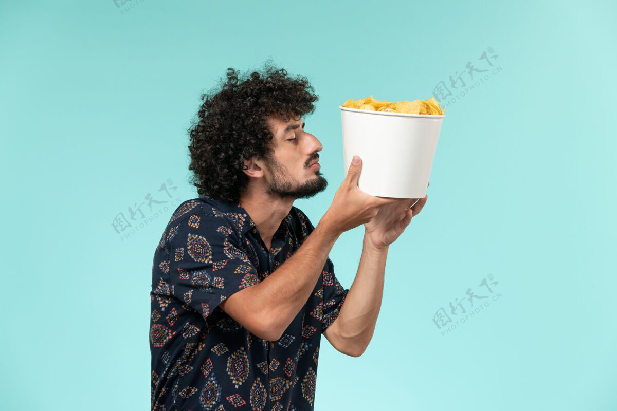 年轻人前视图年轻人拿着土豆cips在浅蓝色的墙上电影院电影院男扩音器喝酒电影