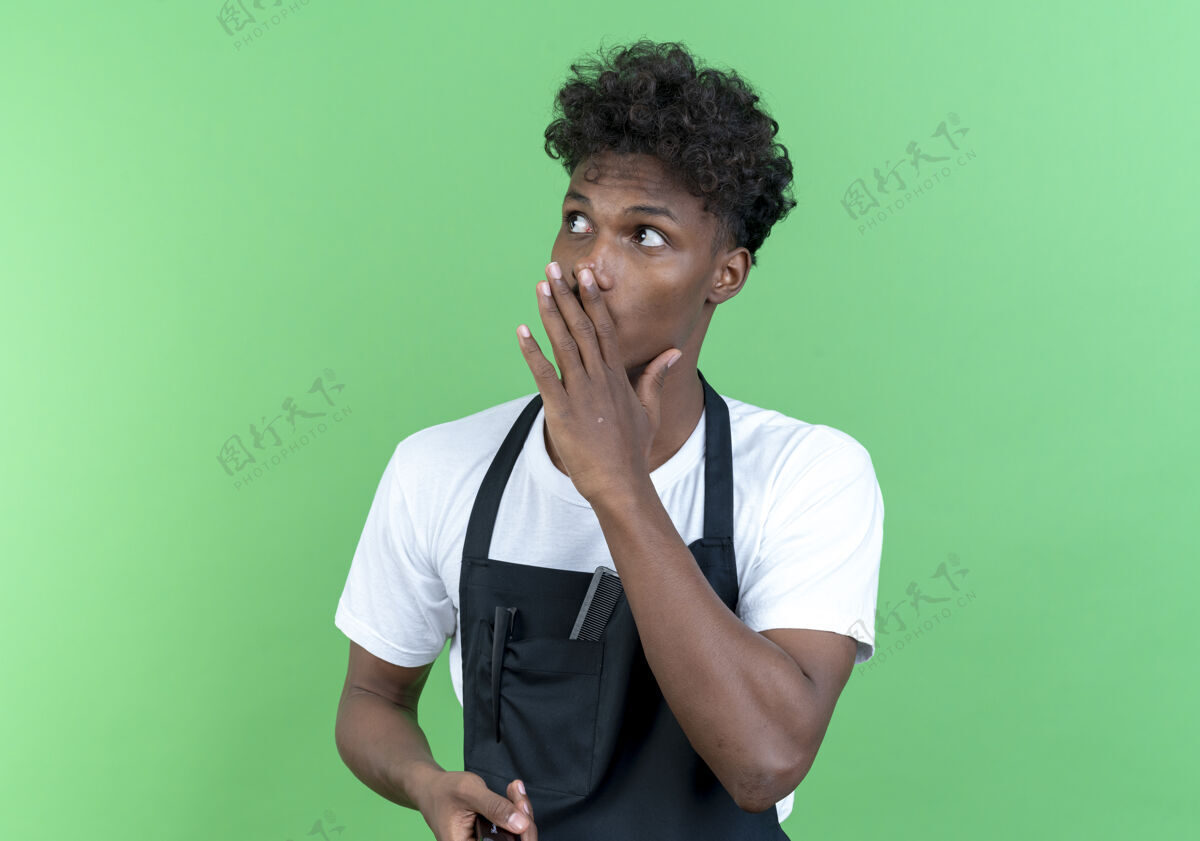 年轻看着身边年轻的美国黑人男理发师穿着制服 在绿色的背景上低语着孤立的声音耳语穿非裔美国人