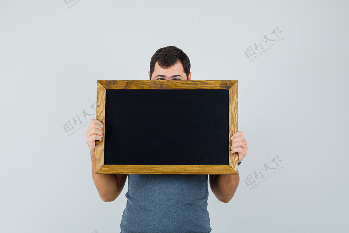 现代穿着灰色t恤的年轻人把脸藏在黑板后面黑板自信朋友