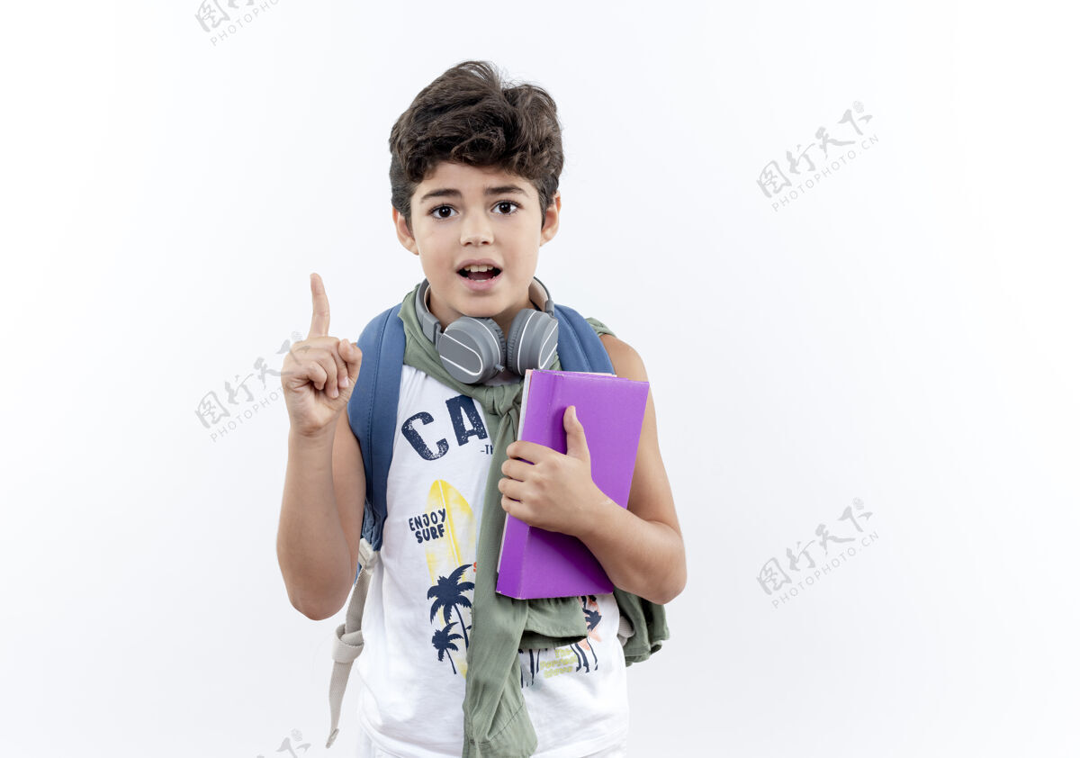 印象印象深刻的小男生背着书包 戴着耳机拿着书 指着上面孤立的白色背景和复印空间小耳机穿