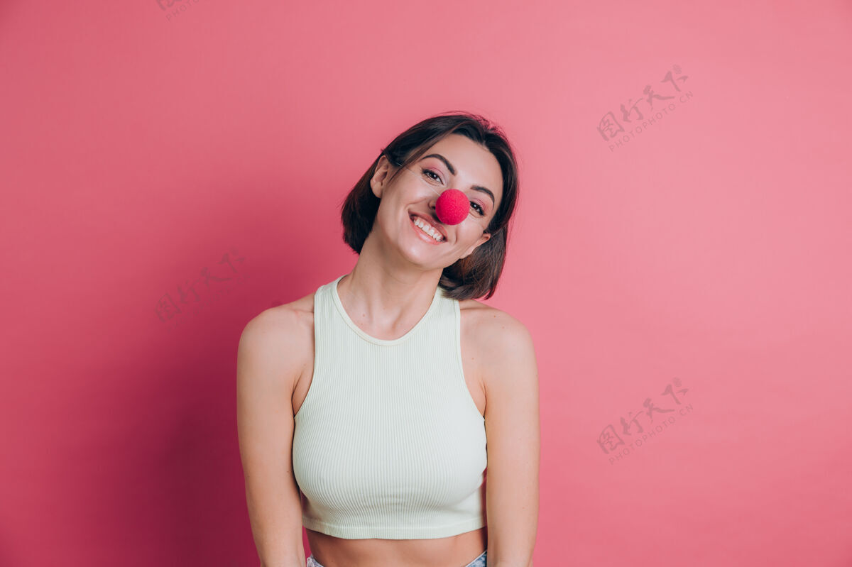 表情粉色背景上的女人挺搞笑 笑容可掬的年轻女子戴着小丑鼻子 派对气氛一个慈善道具
