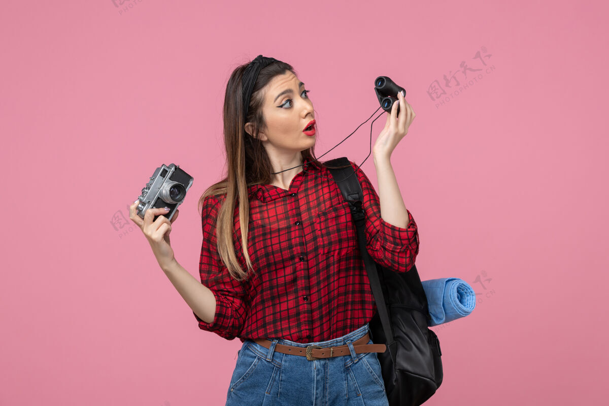 双筒望远镜前视图年轻女性用双筒望远镜和相机在粉红色背景上人类的颜色女人女士头发人类