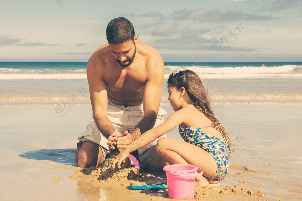 享受可爱的小女孩和她的爸爸在沙滩上建造沙堡 坐在潮湿的沙滩上 享受假期海洋父亲男人