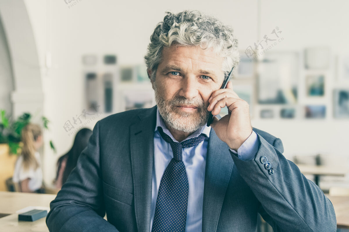 电话成功的成熟商人用手机交谈 站在同事面前 靠在办公桌上成功通讯首席执行官