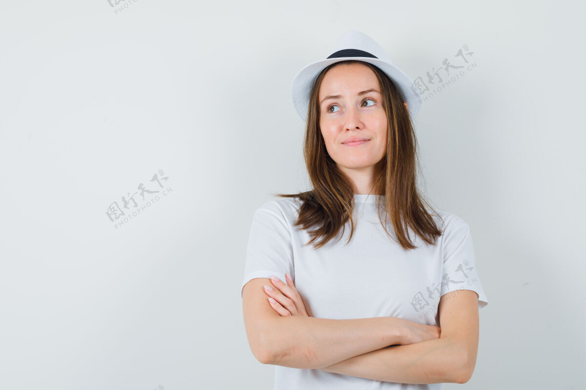 可爱年轻女孩交叉着双臂站在白色t恤帽子里 看起来很梦幻小快乐头发