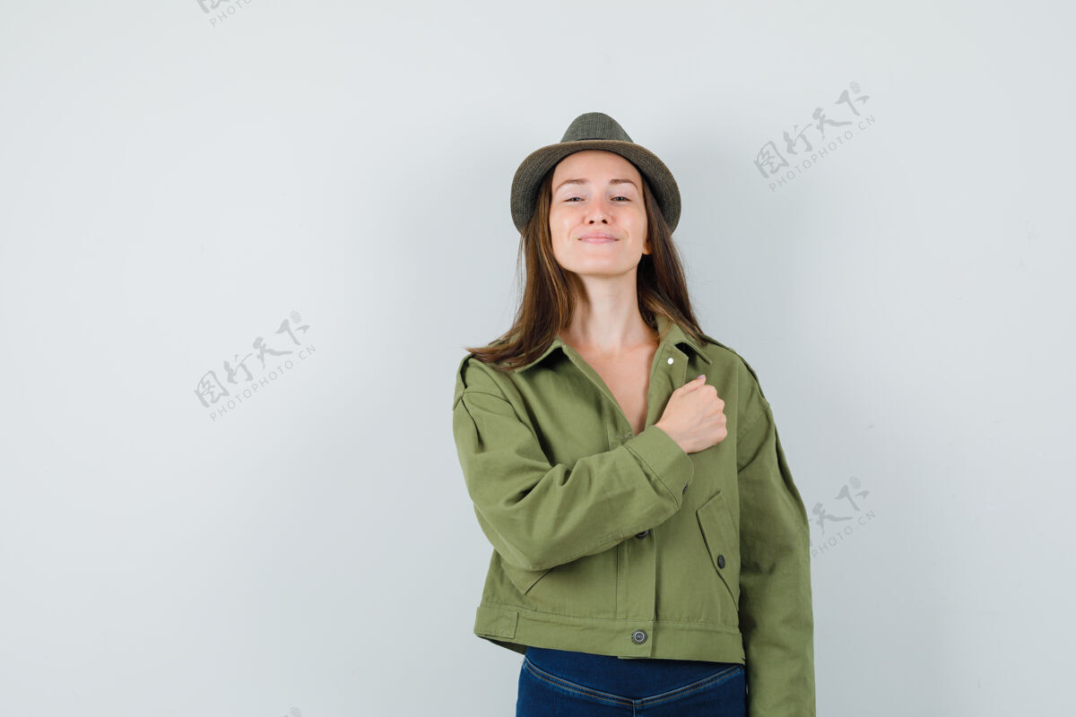 拳头穿着夹克 裤子 帽子的年轻女士用拳头顶着胸膛 看上去很自信时尚兴奋连衣裙