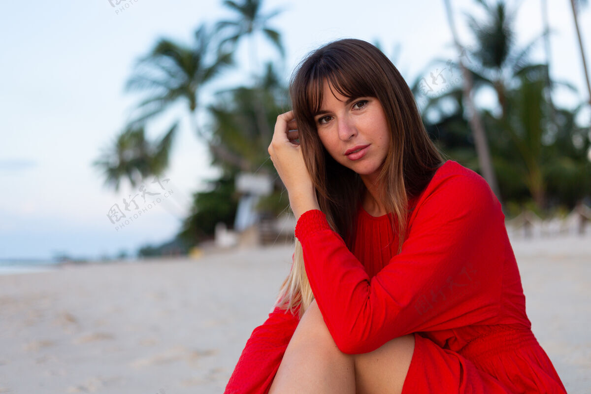 自然日落时分 在热带白色沙滩上 身着红色夏装的白种人女人洋溢着浪漫快乐的心情奢华度假脸庞