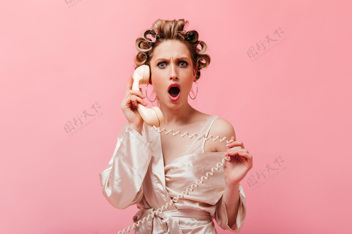 时尚一位卷发的家庭主妇身着丝绸长袍 怒气冲冲地站在前面打电话家庭主妇享受粉色