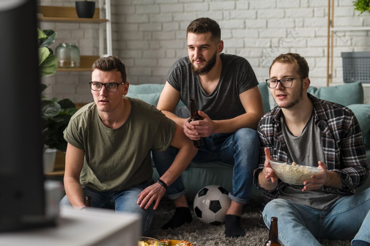 看电视三位男性朋友一边喝啤酒 一边吃零食 一边看电视上的体育节目啤酒瓶伙伴啤酒