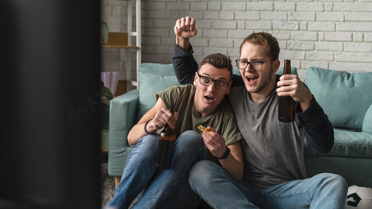 伙伴两个快乐的男性朋友在电视上看体育节目 喝啤酒啤酒看电视电视
