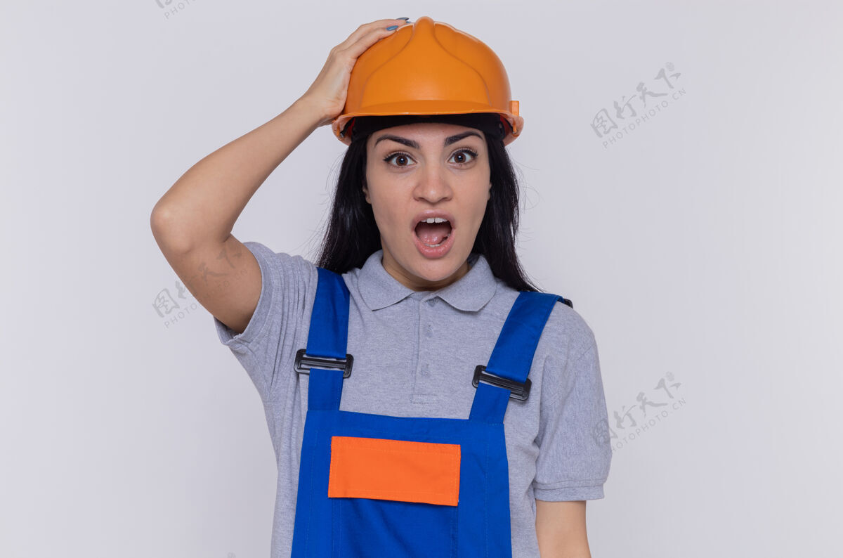 安全身穿建筑制服 头戴安全帽的年轻建筑工人站在白色的墙壁上 惊讶地看着前面头盔惊喜年轻