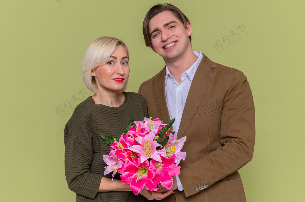 庆祝年轻美丽的情侣幸福的男人和女人用花束拥抱幸福的爱情一起微笑着庆祝国际妇女节站在绿色的墙上美丽男人女人