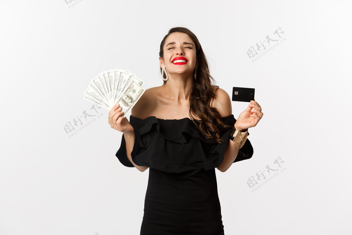 黑发美丽和购物理念满意的年轻女子穿着时尚的衣服 看起来很高兴 拿着信用卡和钱 站在白色的背景下服饰女性魅力