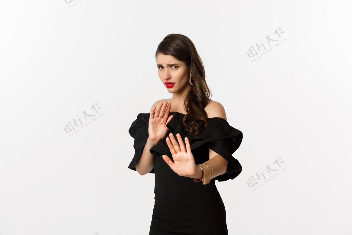 服装时尚和美丽不情愿和担心的女人要求远离 显示停止的手势 看起来很害怕 站在白色背景的黑色礼服年轻拒绝美丽