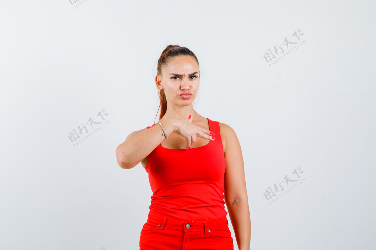 华丽年轻女子展示手枪手标志在红色背心 裤子和看起来自信 前视图商务人物休闲