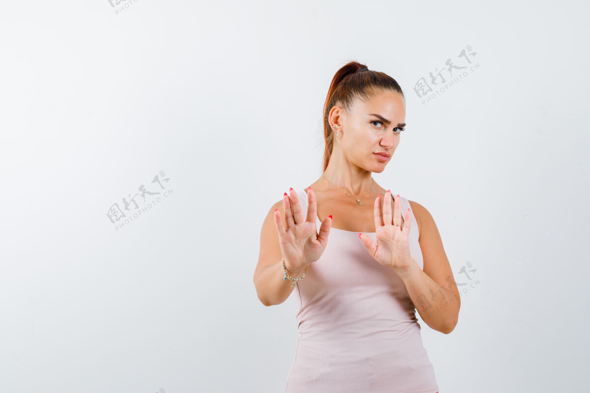 显示身穿白色背心的年轻女性 双手呈投降姿态 表情严肃 正面视图年轻黑发模特