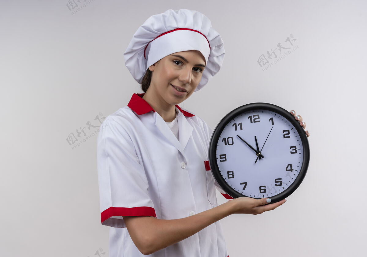 空间穿着厨师制服的年轻快乐的白人厨师女孩拿着白色的时钟和复印空间请等待时钟
