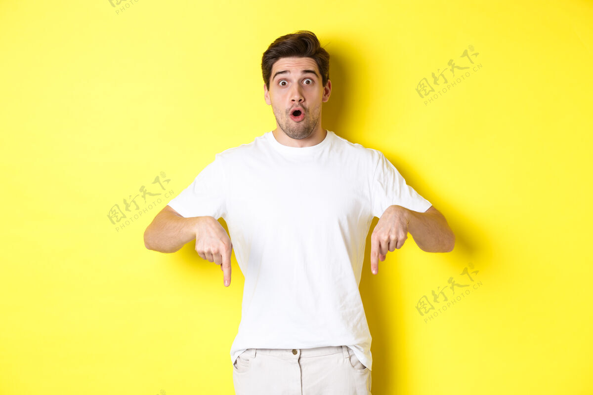黄色印象深刻的家伙手指向下 喘息惊讶地看着相机 站在黄色的背景上自信男人男人