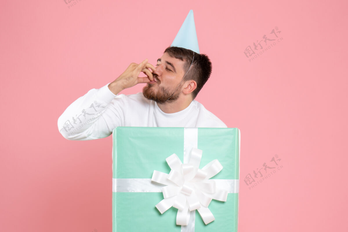 聚会正面图：年轻男性站在礼品盒内 脸上洋溢着喜悦的粉色照片色彩的情感圣诞睡衣派对颜色展台礼物