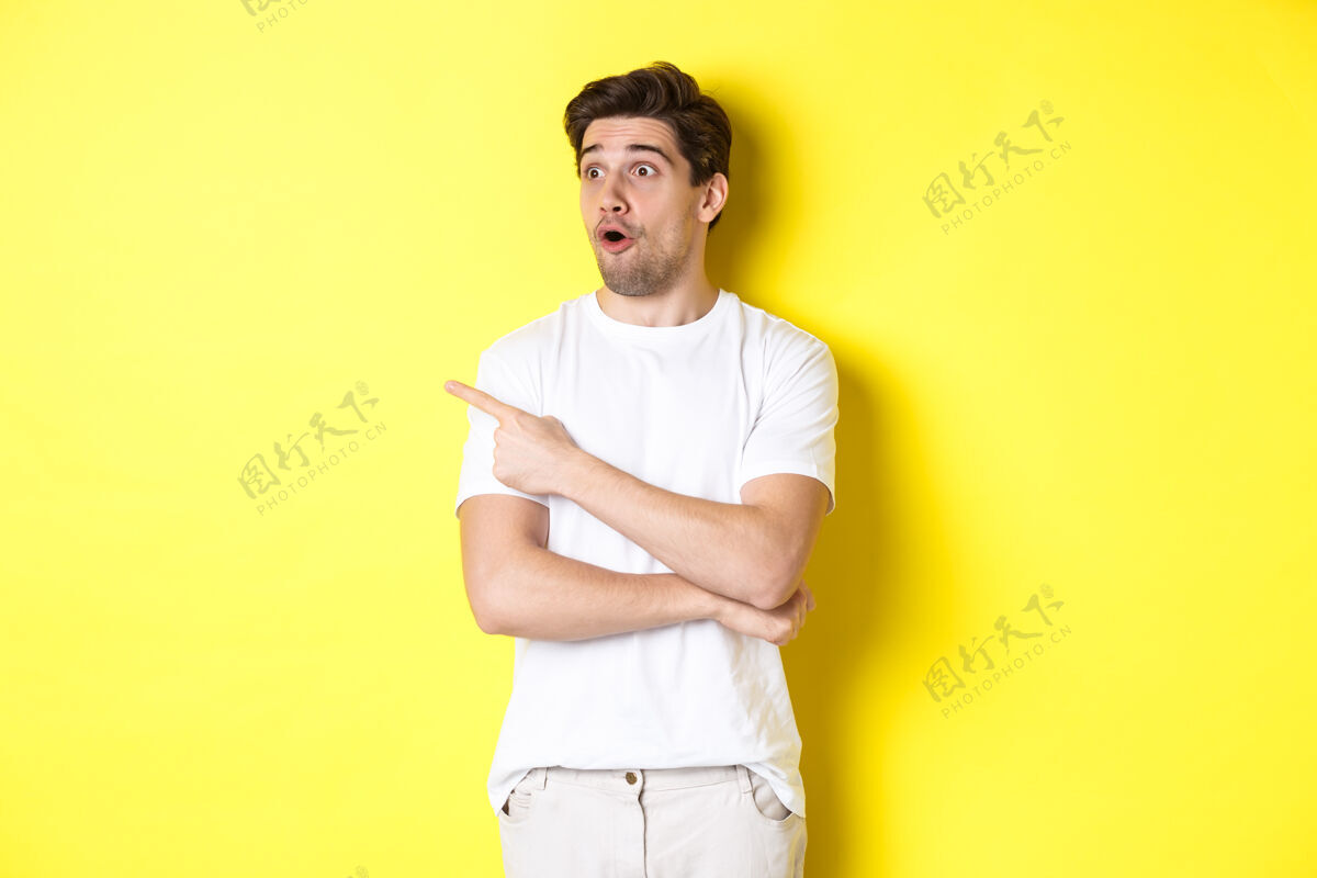黄色一个穿着白色t恤的男人站在黄色的背景下 看着并用手指着宣传片 查看广告帅年轻自信