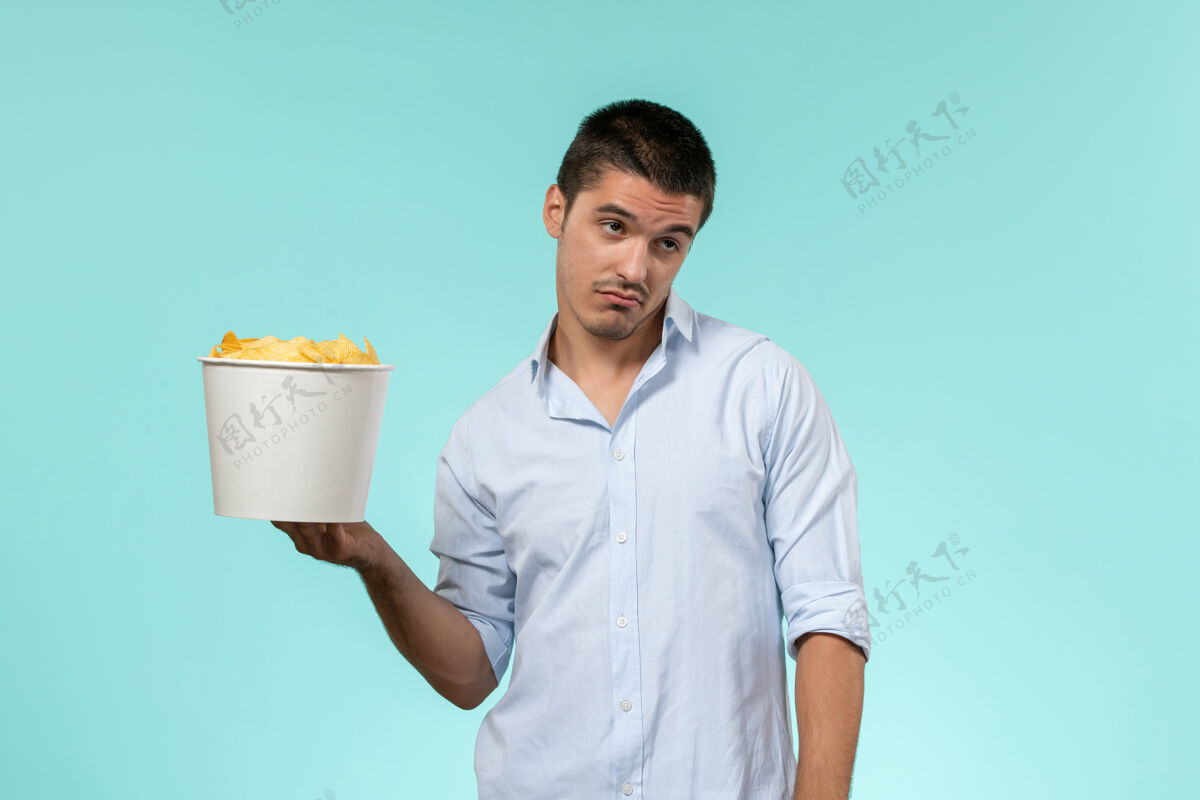 篮子正面图：年轻的男性手拿篮子 浅蓝色的表面上放着薯片远程土豆持有