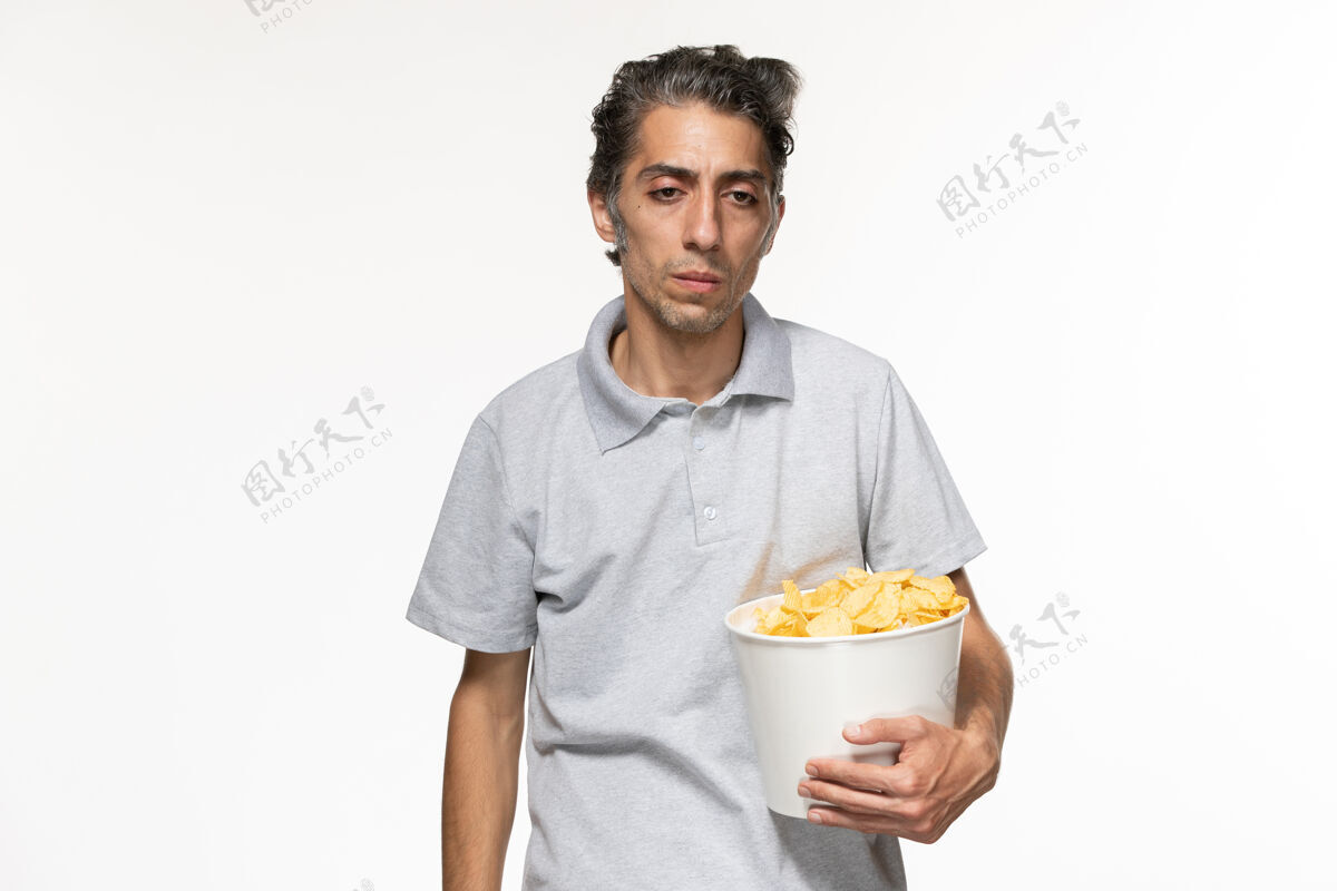 土豆正面图：年轻的男性拿着一个装着薯片的篮子 白色的表面上有压力远程年轻的男性男