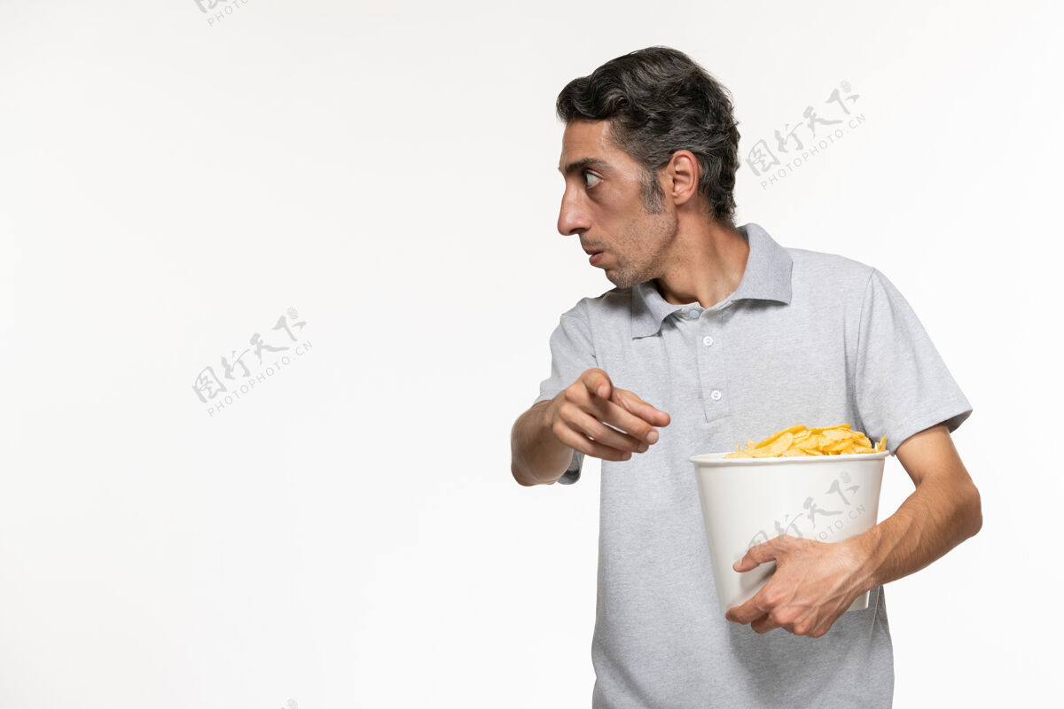 衣服正面图：年轻的男性拿着一个装着薯片的篮子 在一个白色的表面上与人交谈电影院某人土豆